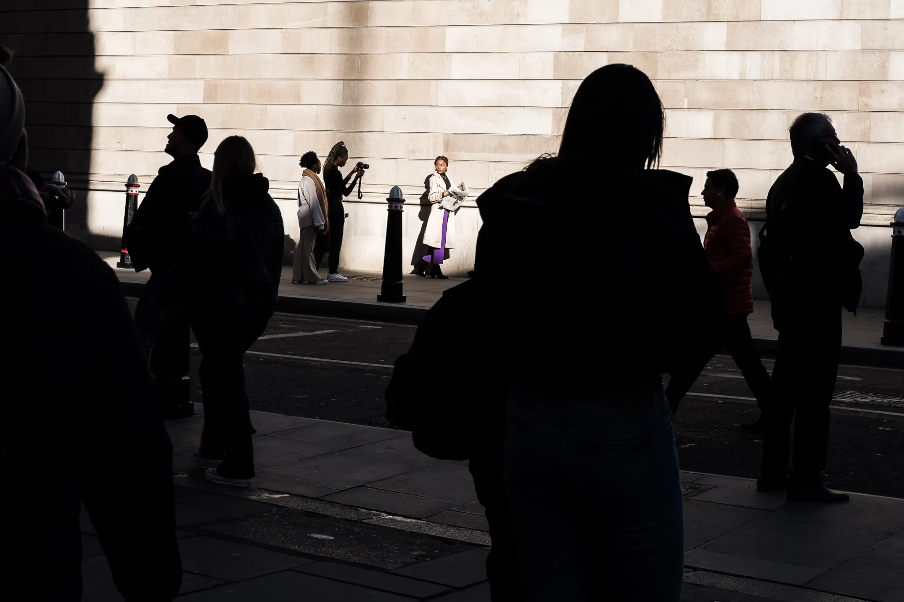 Sun lit woman posing newspaper in hand silhouetted pedestrians walk by