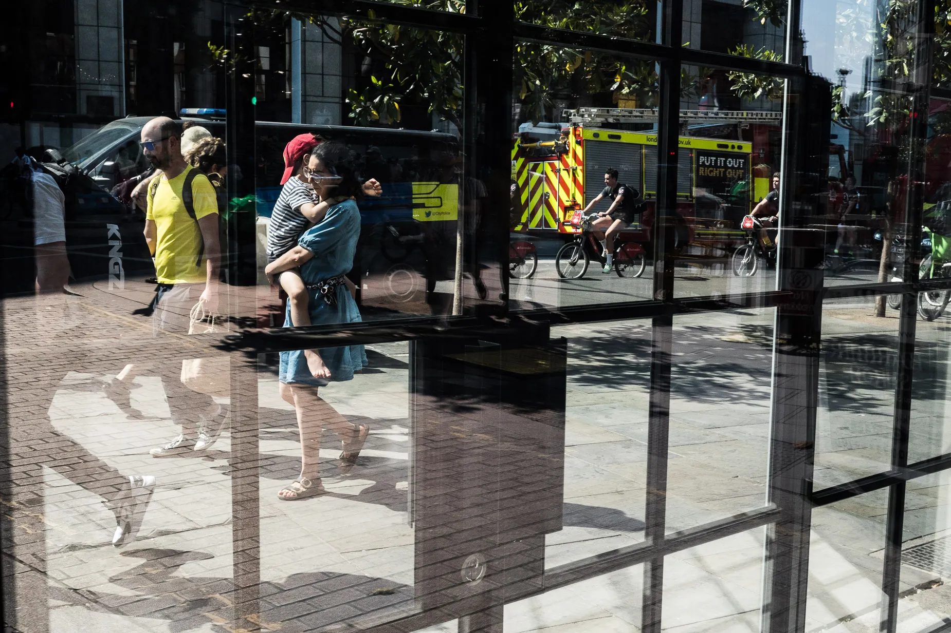 woman carries shoeless toddler amidst cyclist, pedestrians and traffic