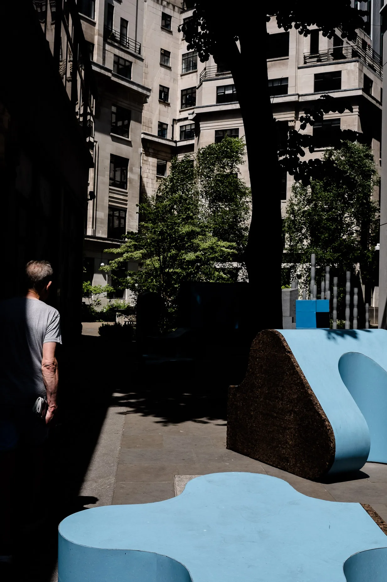 Light & shadow scene of tree, against stone building with light blue blocks in foreground