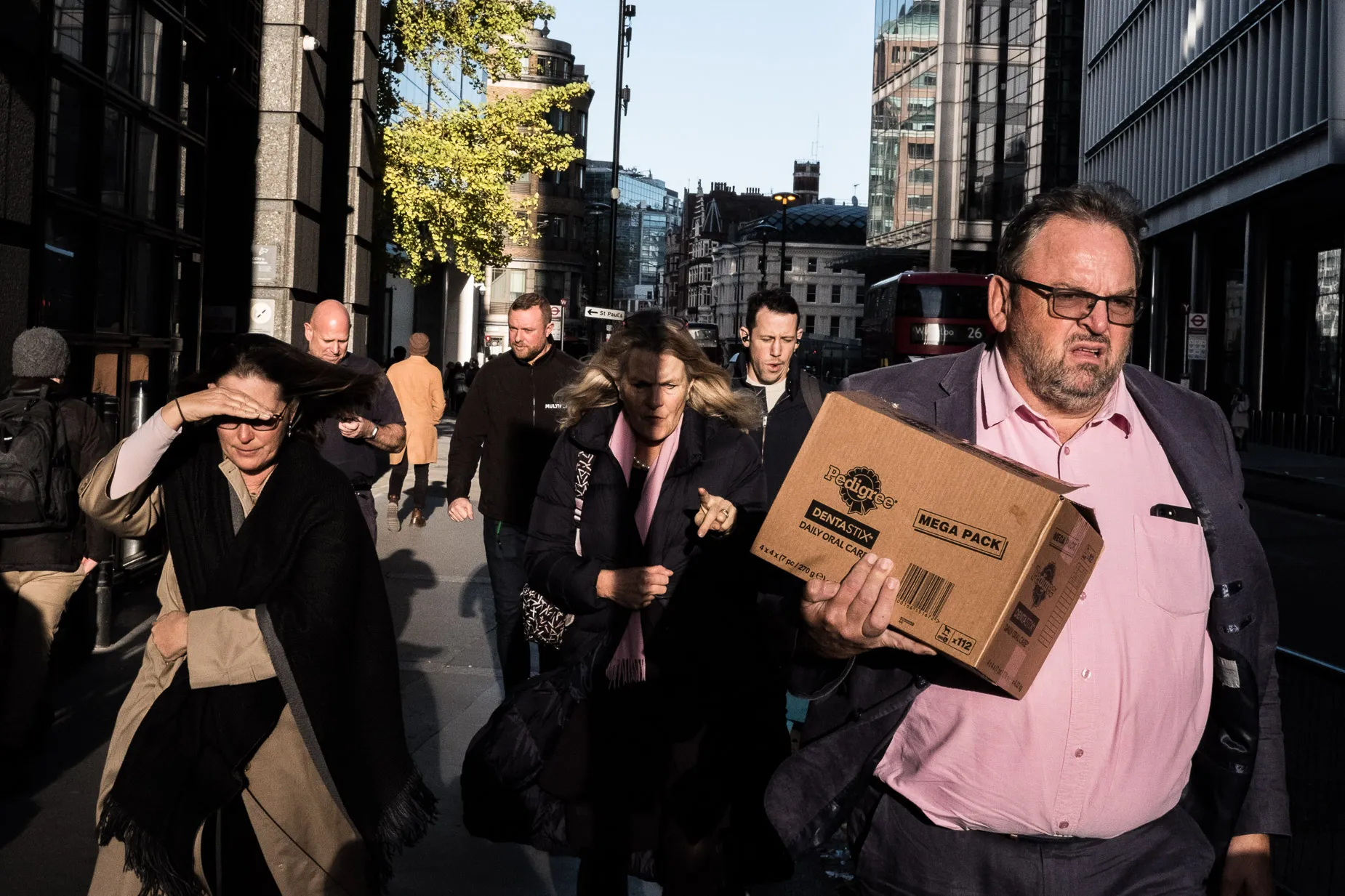 Street scene city people walking into direct sun light man with cardboard box