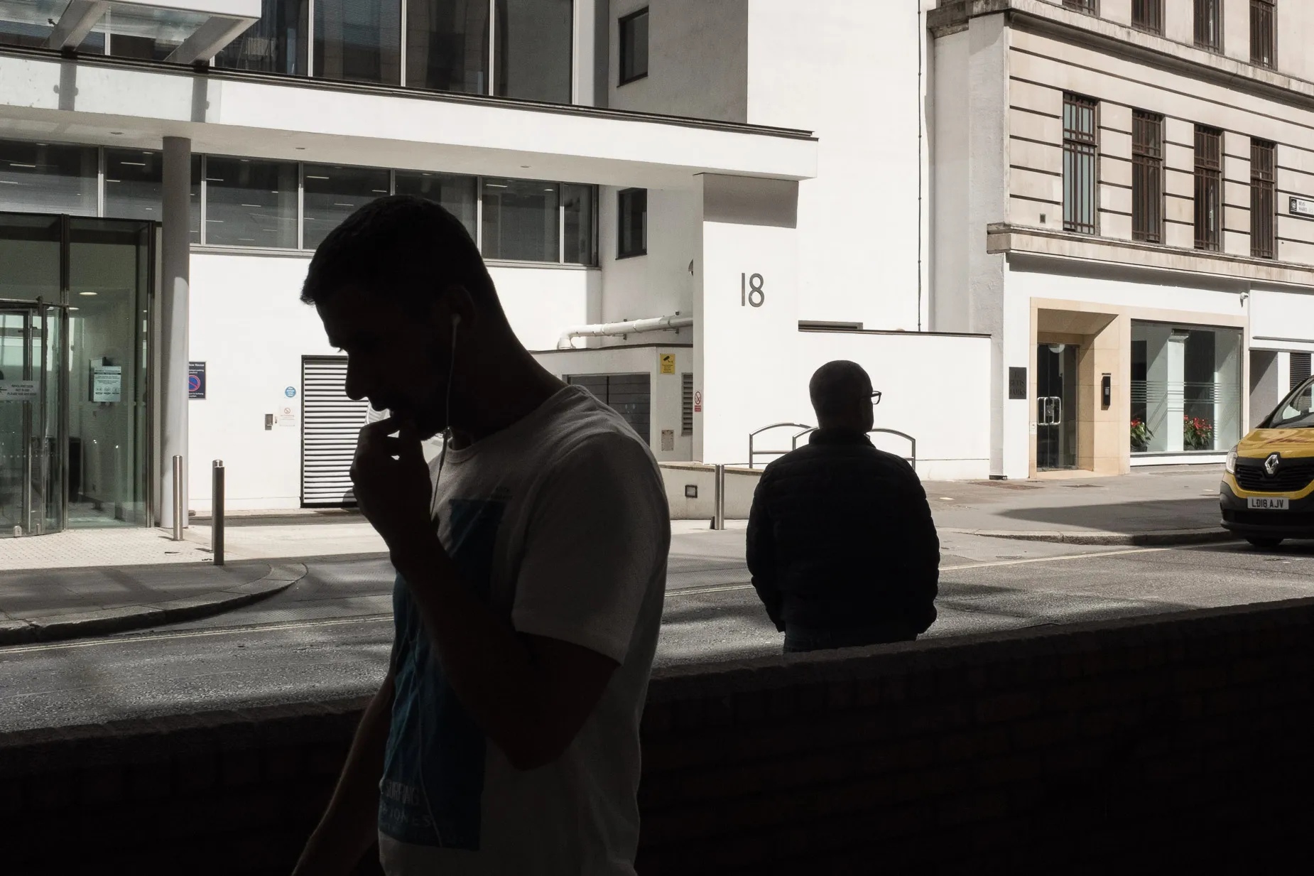 Light and shadow photograph showing two men silhouetted against a white building