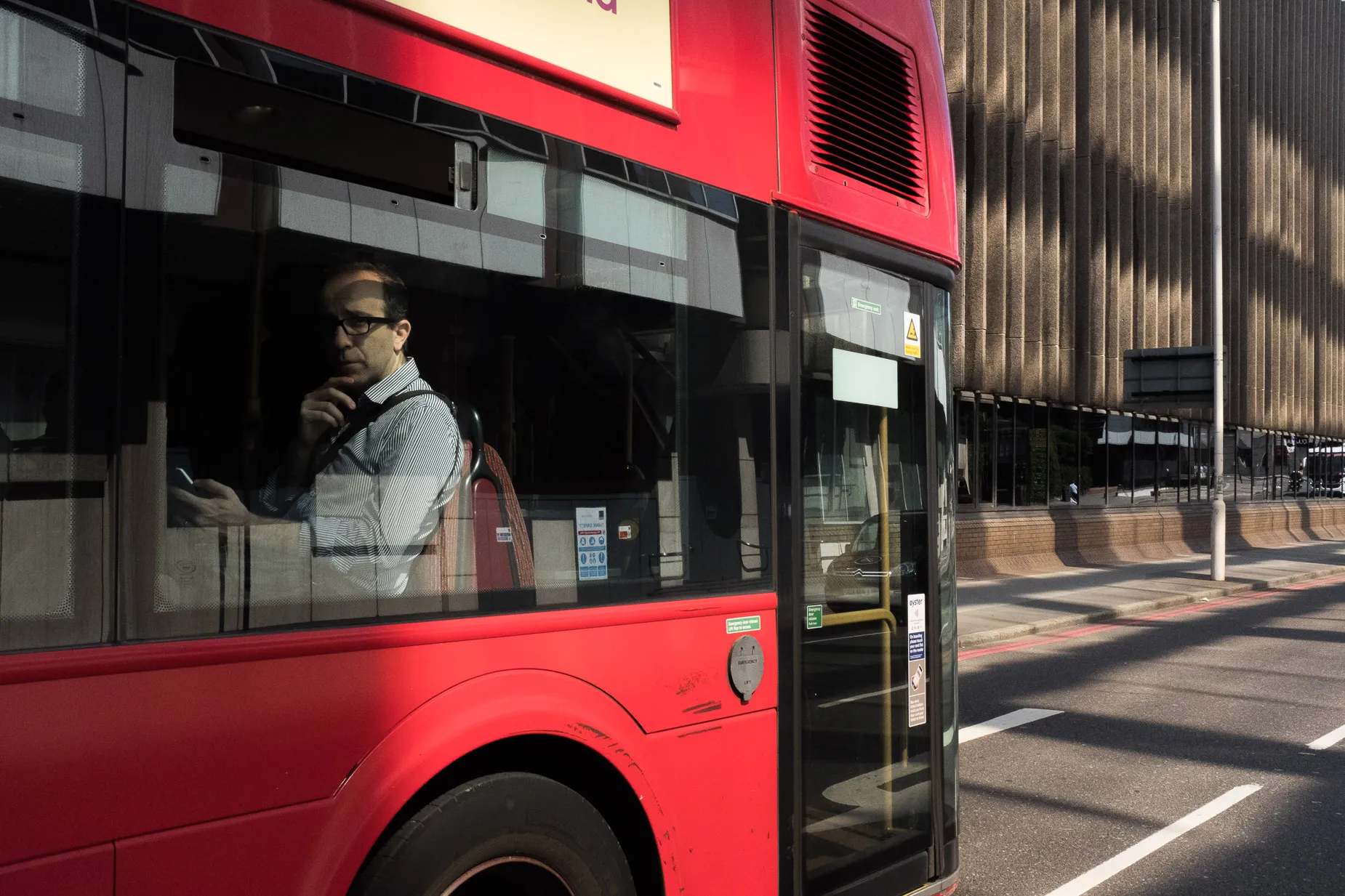 Man on bus pensively looking at phone turns to meet the camera