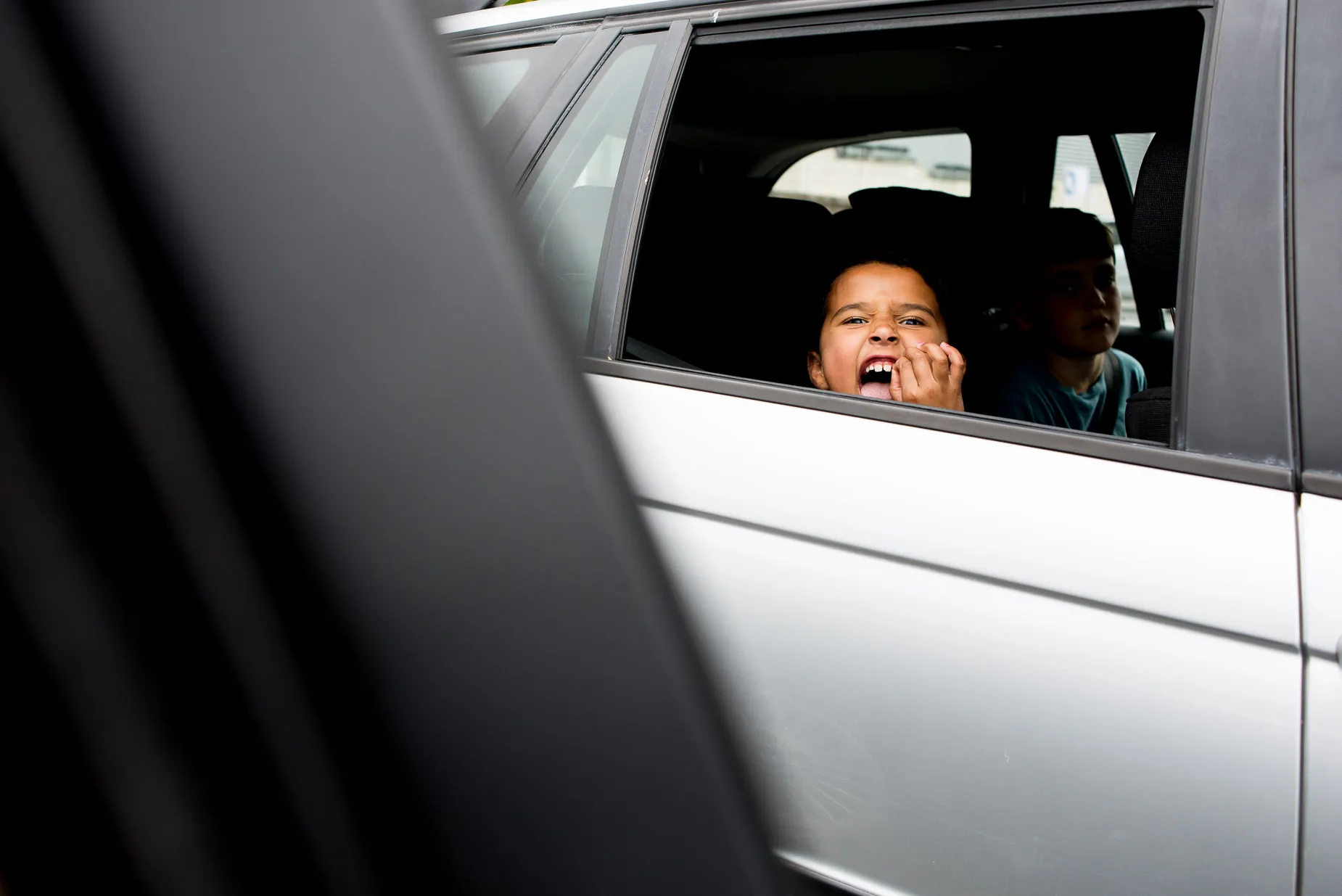 Young girl wiggles loose tooth from rear of car window