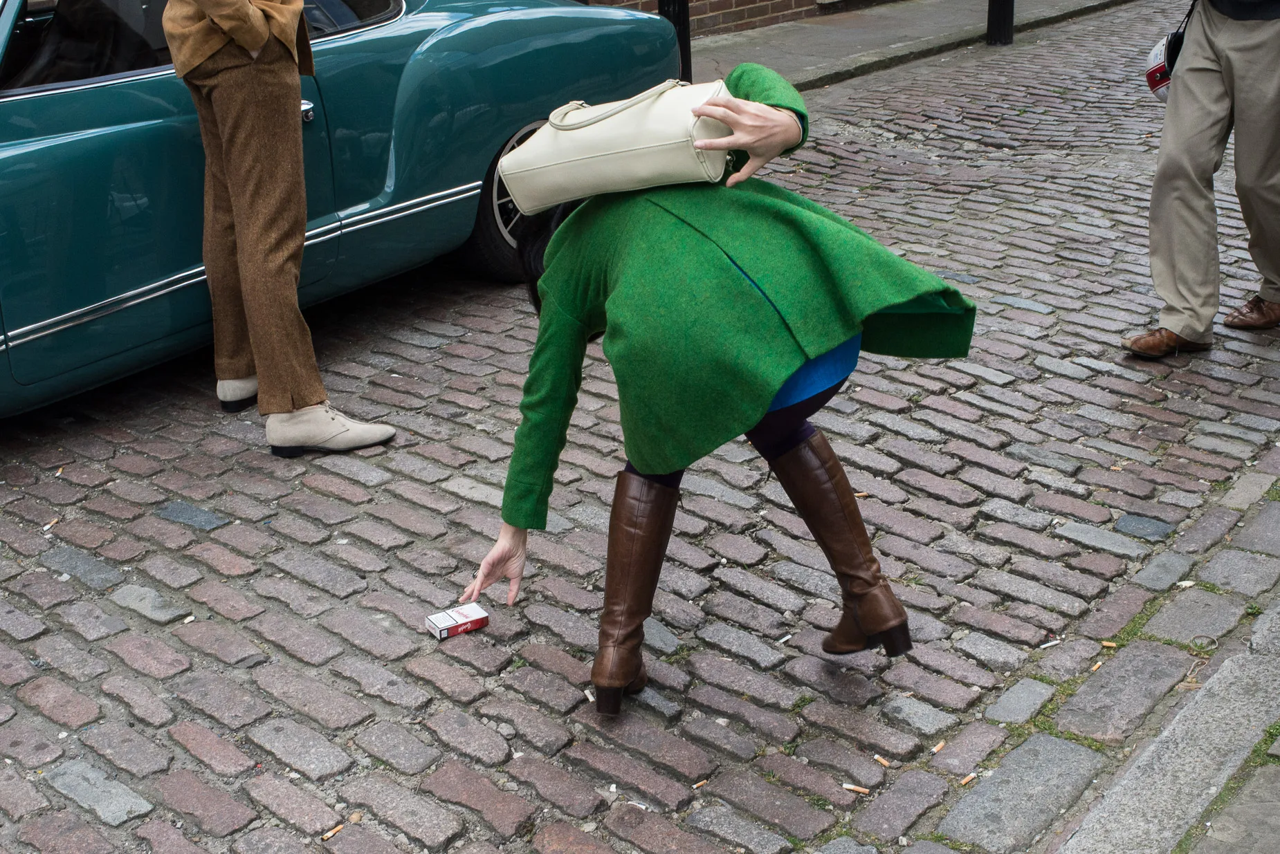 Woman tries to pick up cigarette packet her other arm clutches hand bag