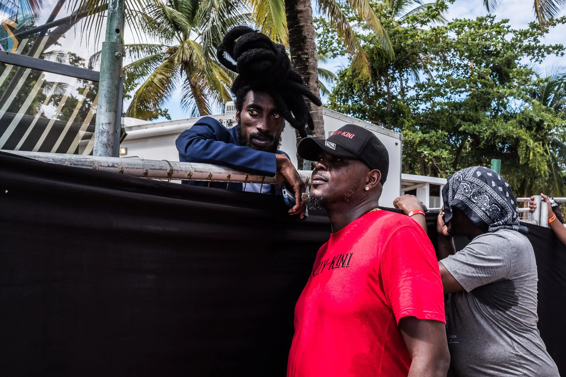 Dread locked man talks to friend over a barrier at a beach party
